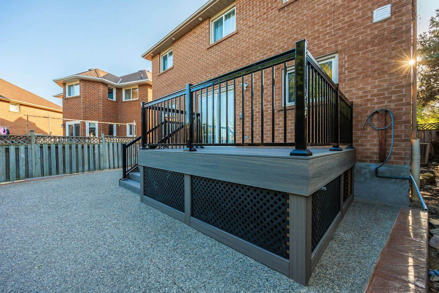 A raised backyard deck against a brick house, with a fenced side yard beyond.