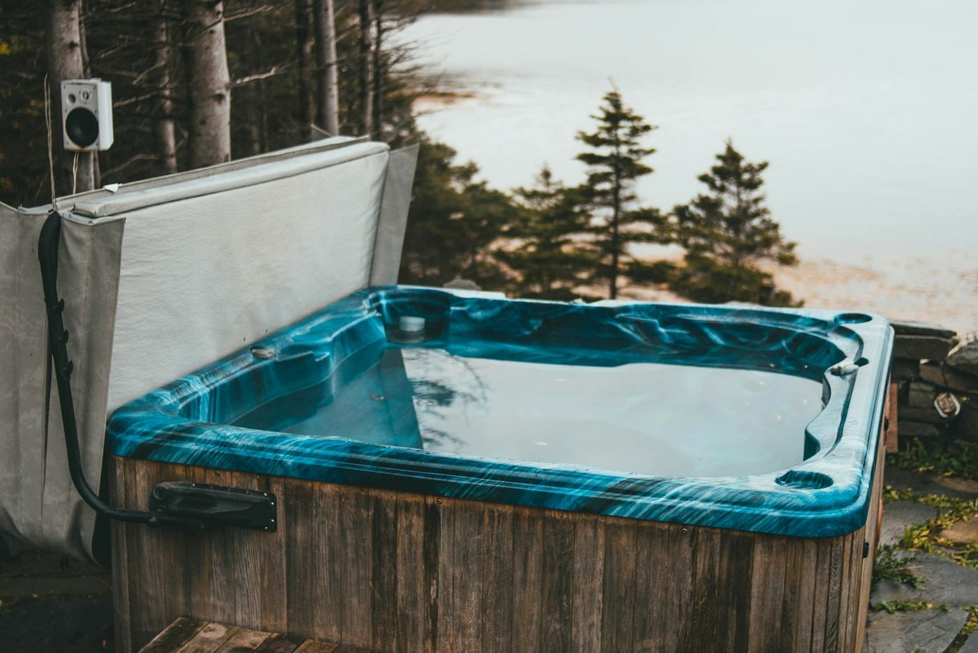 A weathered acrylic hot tub with its cover propped open, sitting on a stone patio.